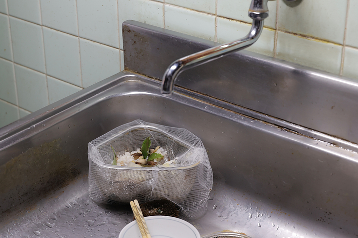 ステンレス製のシンクに設置された排水口フィルターには、野菜屑などのゴミが溜まっています。蛇口が上部に見えています。