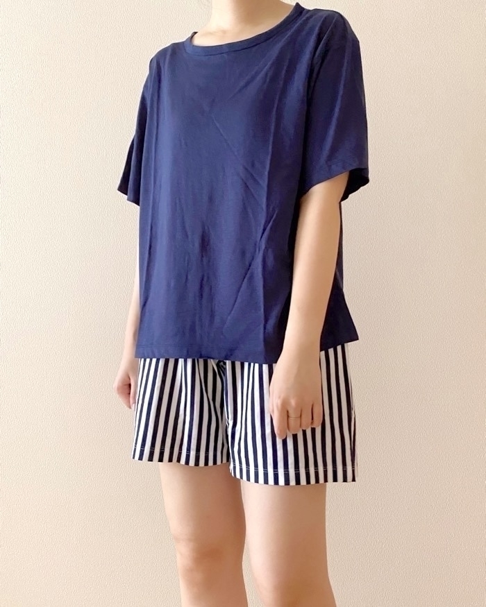A person wearing a plain T-shirt and striped shorts stands against a plain background