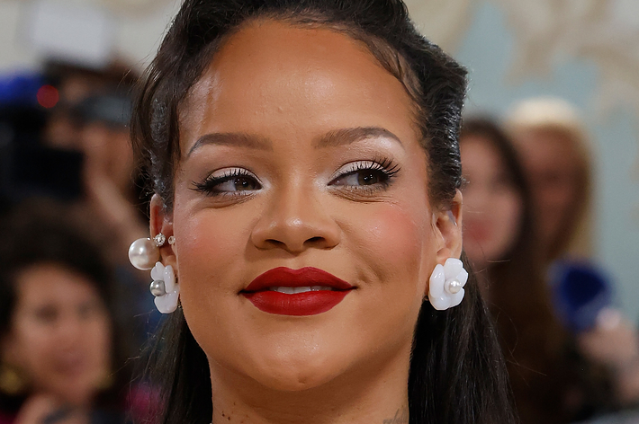 Rihanna smiles wearing a layered pearl necklace and dress with floral details