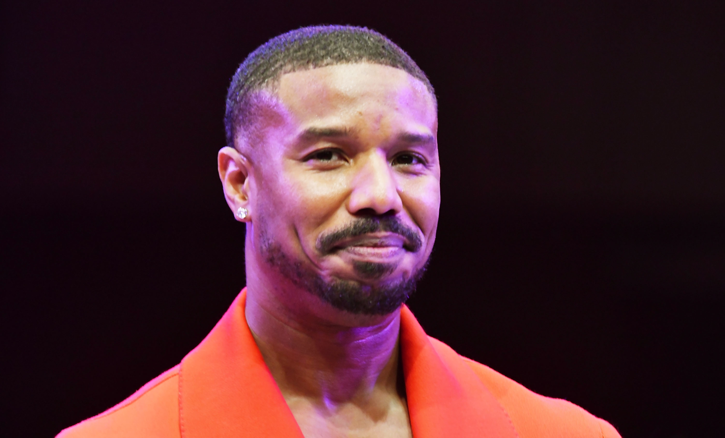 Michael B. Jordan is wearing a tailored suit and smiling at a public event