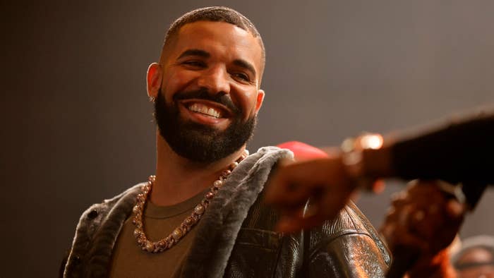 Drake smiling and looking to the side, wearing a casual outfit with a beaded chain necklace