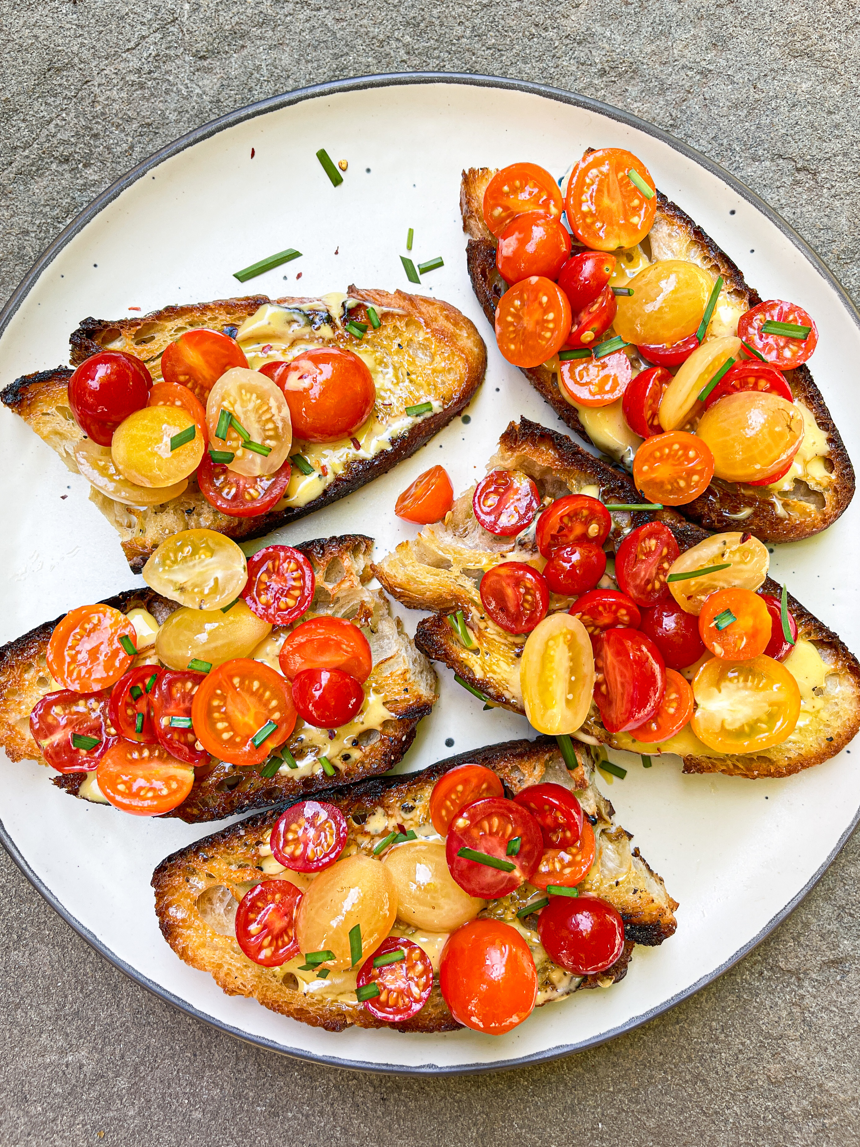 Plate with five slices of toasted bread topped with cherry tomatoes, herbs, and a creamy spread