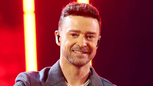 Justin Timberlake is performing on stage, wearing a suit jacket and a pearl necklace, with a red stage light background