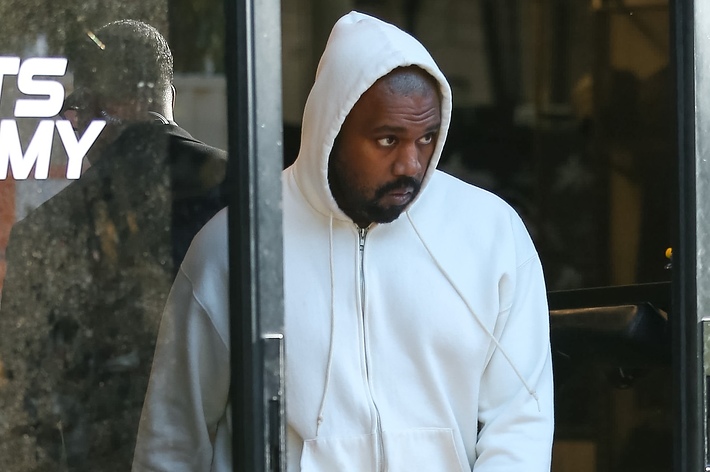 Kanye West in a white hoodie, looking away while exiting a building