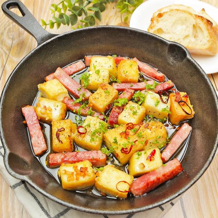 鋳鉄製のフライパンに料理がテーブルに置かれています。背景にはパンのスライスが見えます。