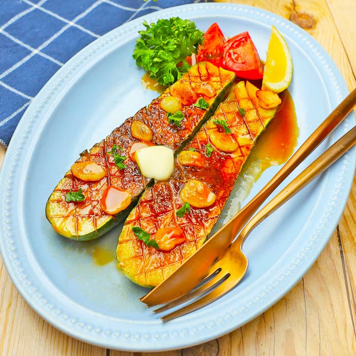 お皿に盛られたグリルドズッキーニ、上にガーリックとバターが乗り、パセリとトマトの付け合わせが添えられています。