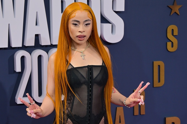 Ice Spice poses on the red carpet wearing a sheer black outfit and holding up peace signs at a music awards event
