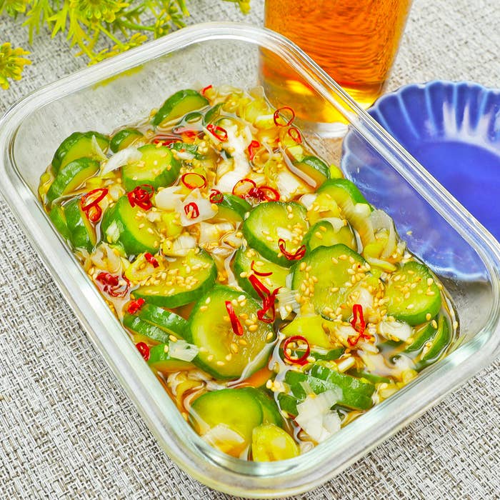 ガラス容器に盛られた野菜のマリネ、薄切りキュウリと赤唐辛子が入っており、隣に飲み物と小皿が置かれている。