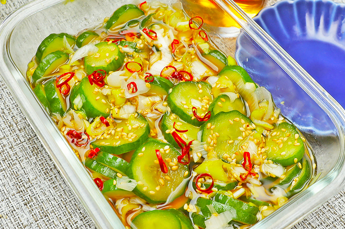 ガラス容器に盛られた野菜のマリネ、薄切りキュウリと赤唐辛子が入っており、隣に飲み物と小皿が置かれている。