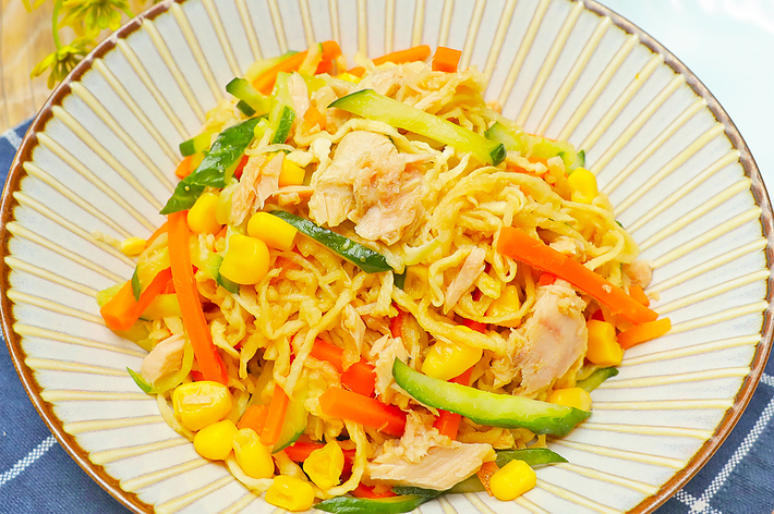 ラーメンサラダの皿には、細切れの鶏肉、きゅうり、にんじん、トウモロコシが盛り付けられています。