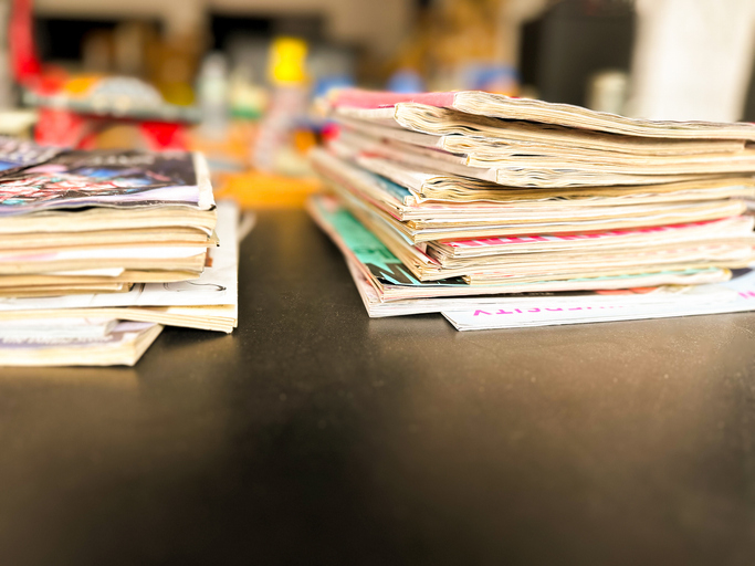 Two stacks of magazines placed on a dark surface with a blurry background