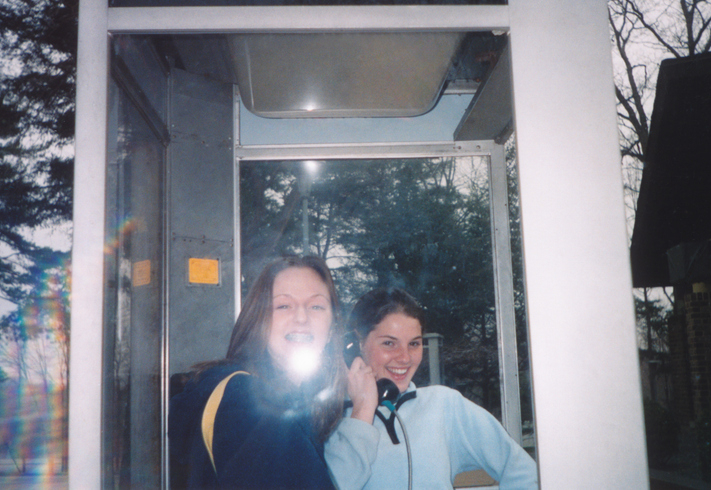 Two smiling people, one holding a phone, inside a phone booth. They appear to be laughing and enjoying the moment. Names unknown