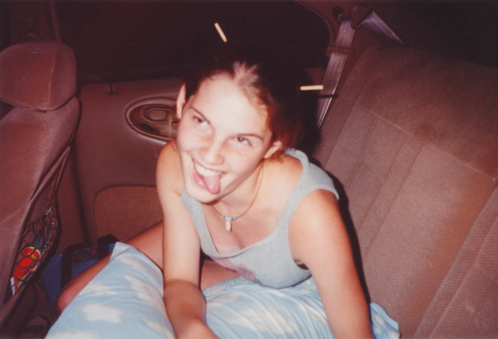A young woman with chopsticks in her hair playfully sticks out her tongue while sitting in the back seat of a car