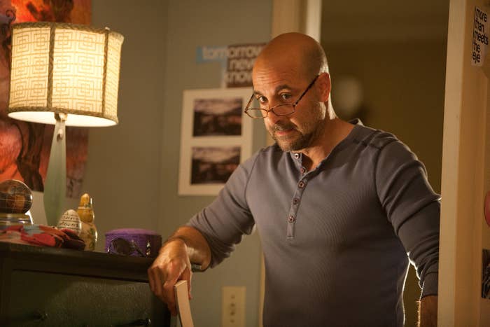 Man with glasses in blue shirt reading a book in a room with a lamp and wall decorations