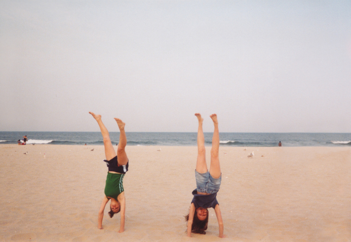 Two people doing handstands on a beach with the ocean in the background