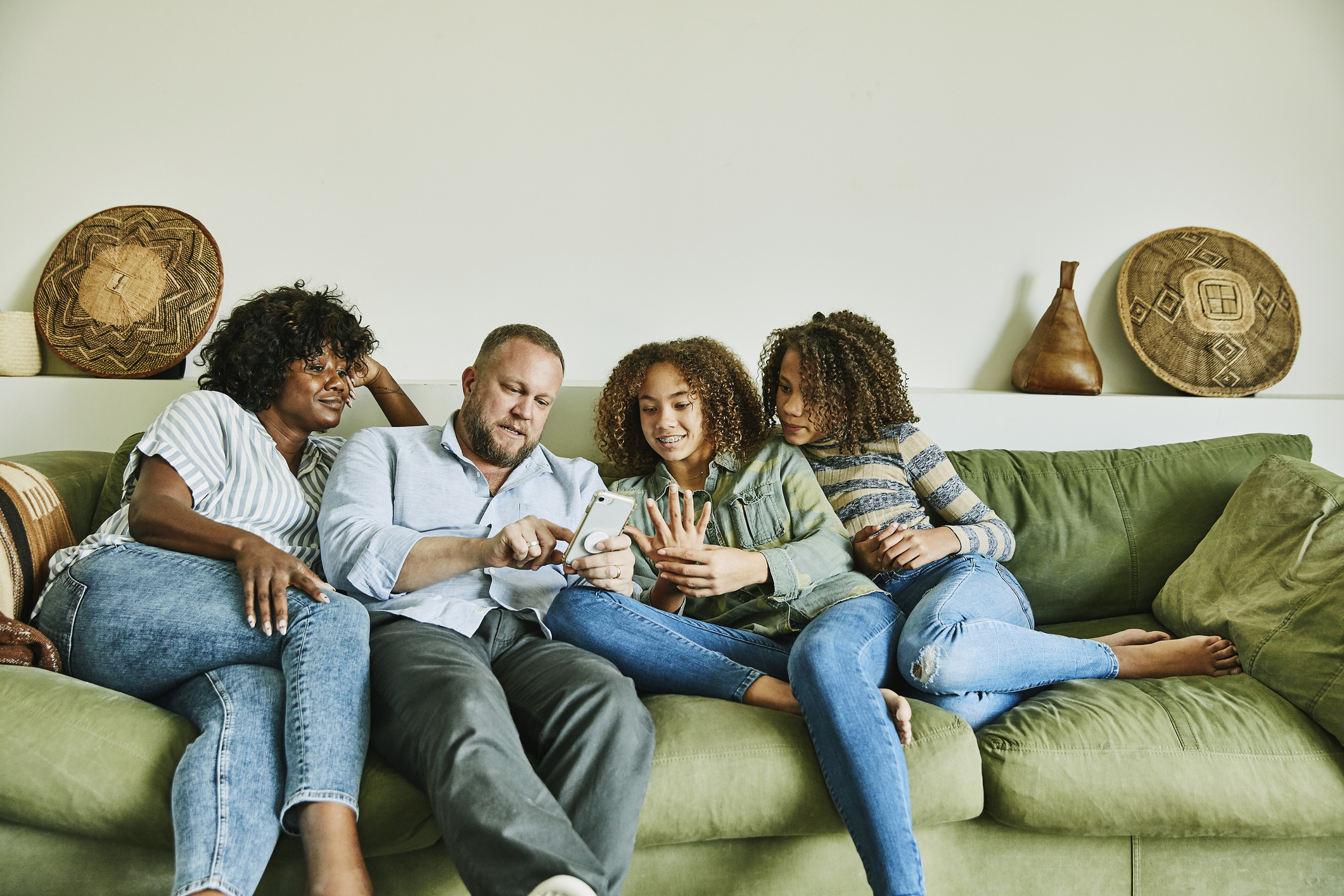 Jakobi Austin, Gary B, Grace and Lena Sabia seated on a green couch, focused on a mobile phone, with decorative items on the wall behind them