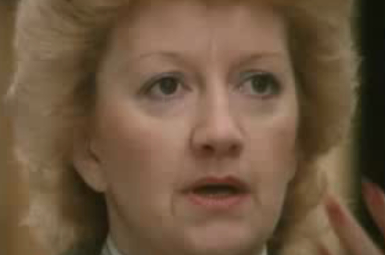 A close-up of an unidentified person with light-colored, voluminous hair and a serious expression