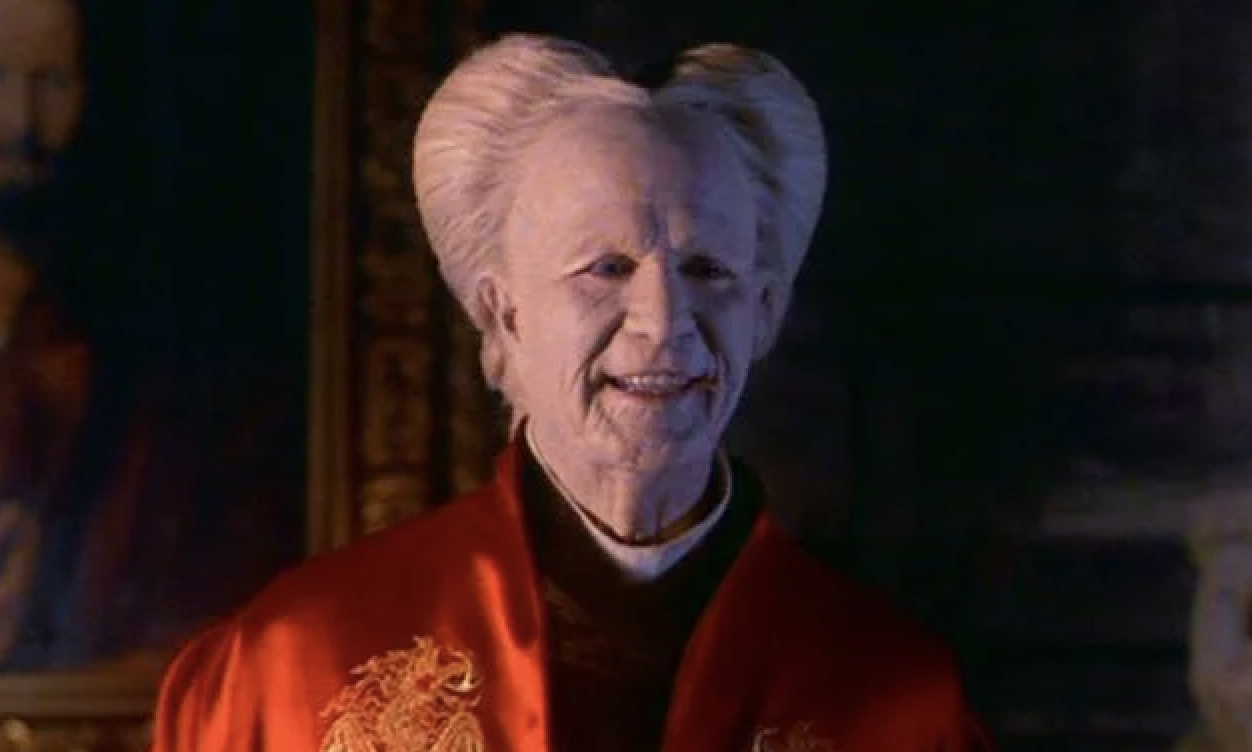 A smiling older man with a high-pomp hairstyle and wearing an elegant robe with dragon embroidery