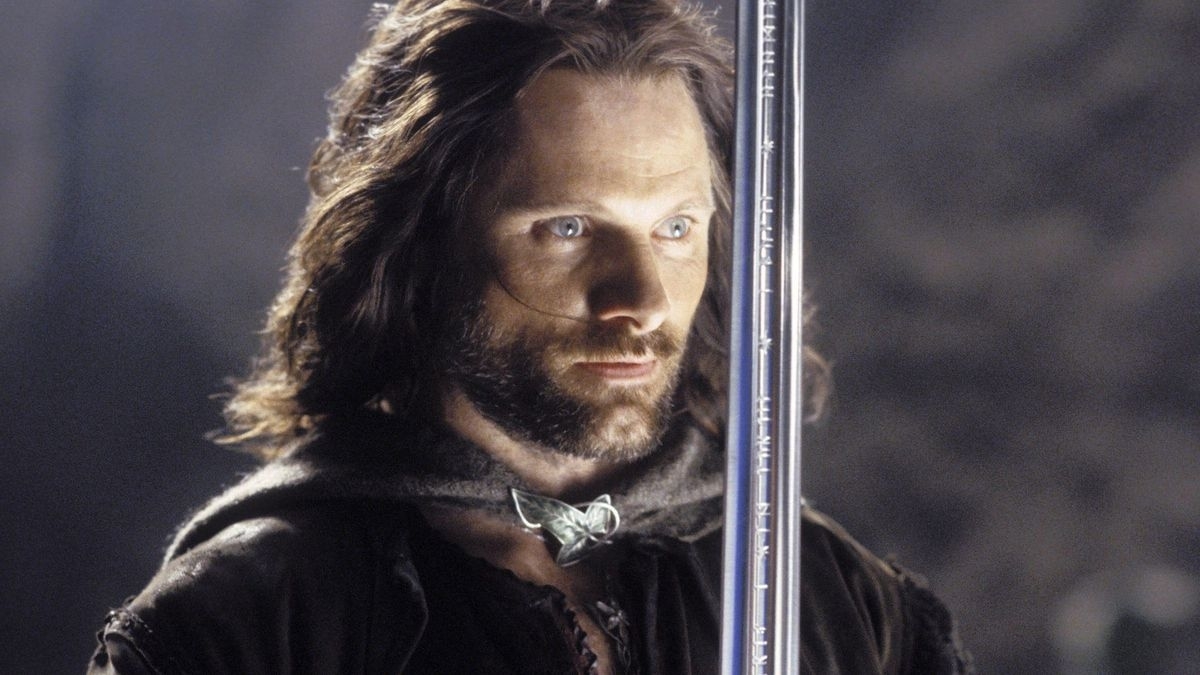 Viggo Mortensen as Aragorn from "The Lord of the Rings," holding a sword and staring intently. He wears medieval-style clothing with a cloak
