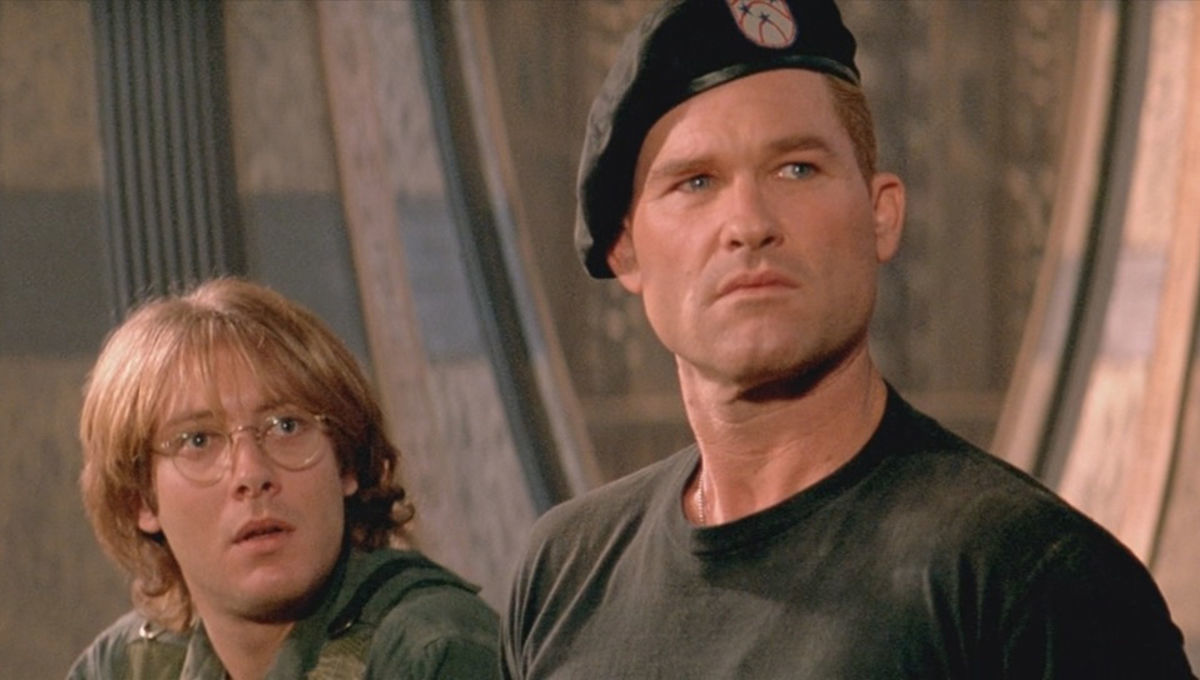James Spader in glasses and military jacket looks surprised beside Kurt Russell in a beret and black shirt in a scene from "Stargate."