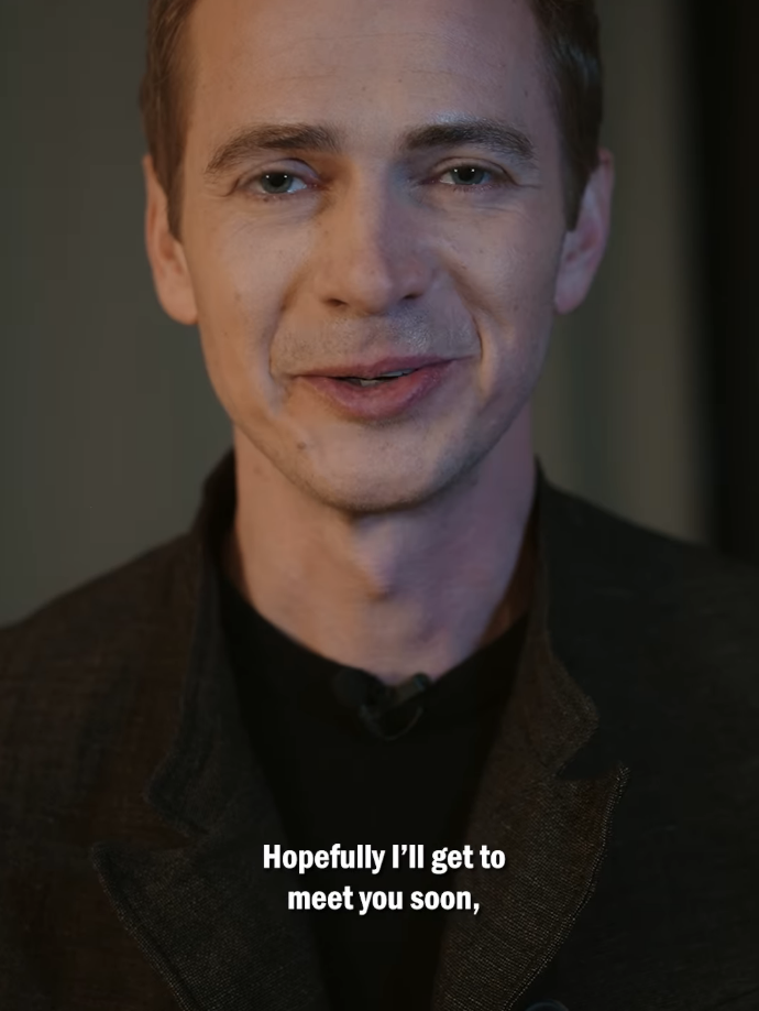 Hayden Christensen is wearing a dark jacket and black shirt. Smiling, he says, &quot;Hopefully I’ll get to meet you soon&quot;
