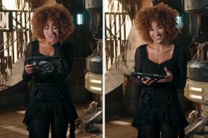 Adassa, in a black ruffled dress, reacts emotionally while reading from a tablet in a rustic, industrial setting