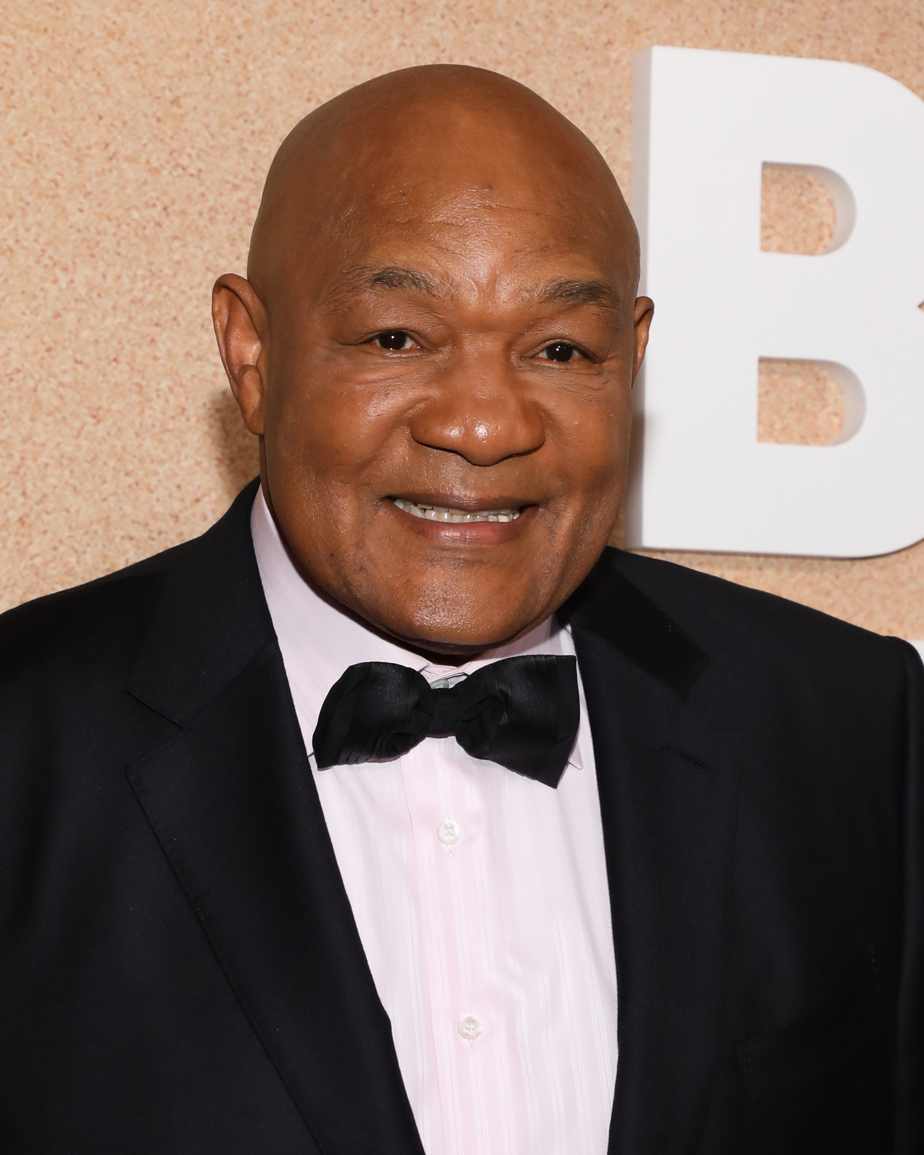George Foreman smiles on the red carpet in a formal suit with a bow tie