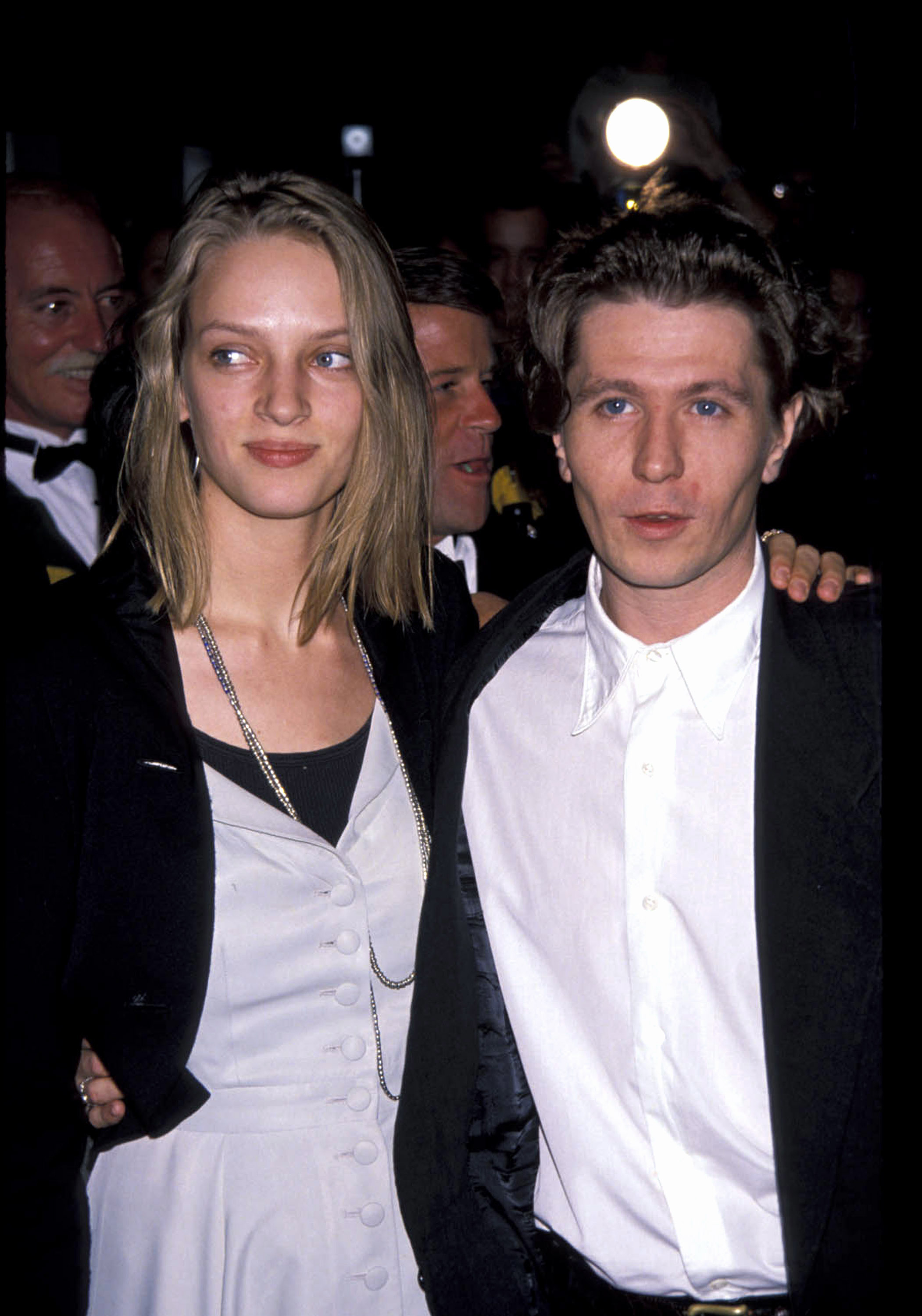 Uma Thurman and Gary Oldman on a formal red carpet event. Uma wears a layered dress with blazer; Gary wears a suit with a white shirt