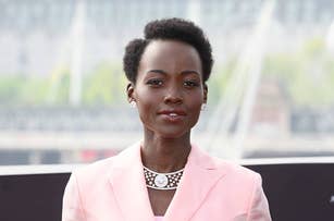 Lupita Nyong'o poses outdoors in a light-colored suit with a croc-styled necklace and earrings