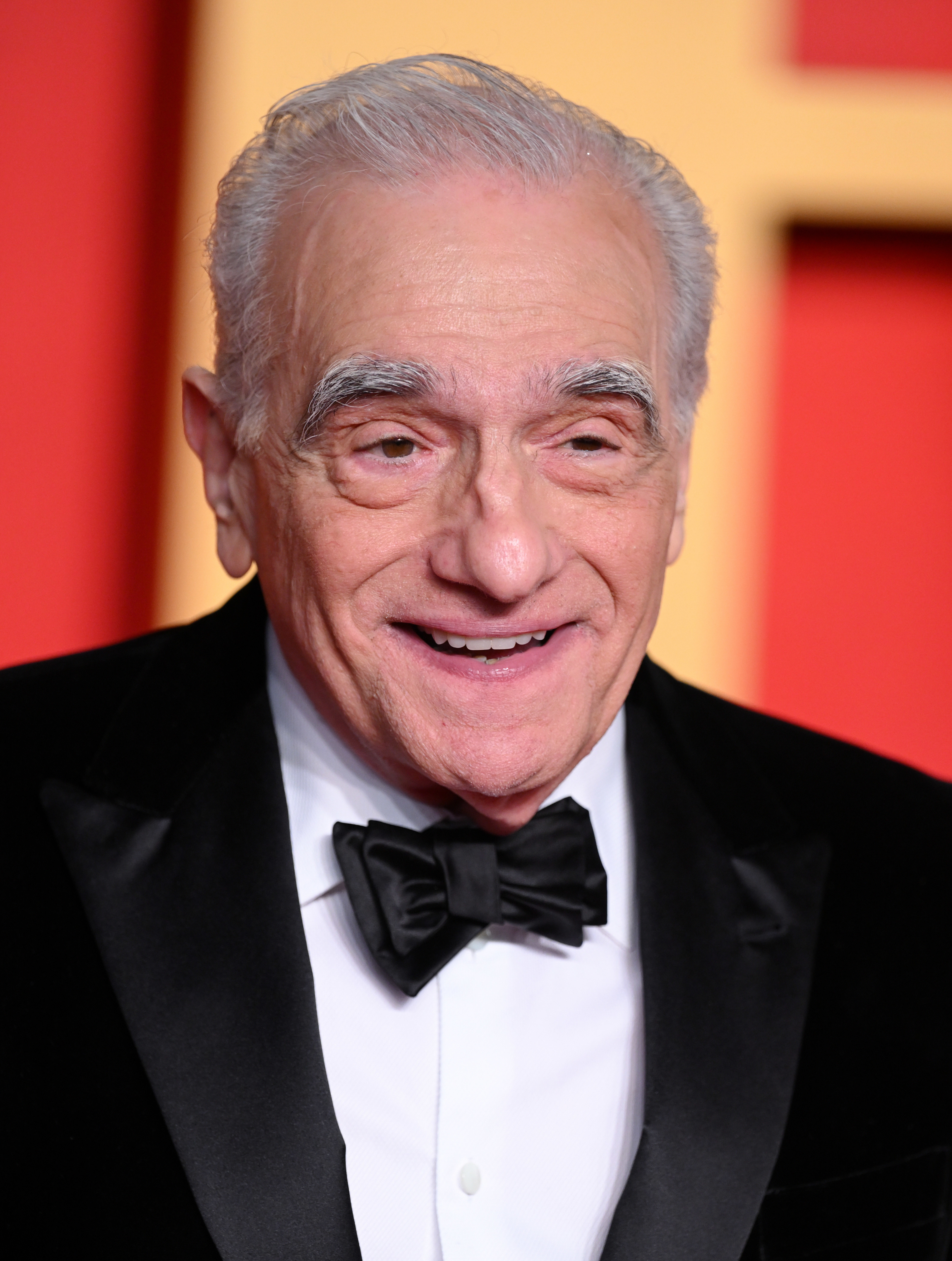 Martin Scorsese smiles while wearing a classic black tuxedo and bow tie at a formal event