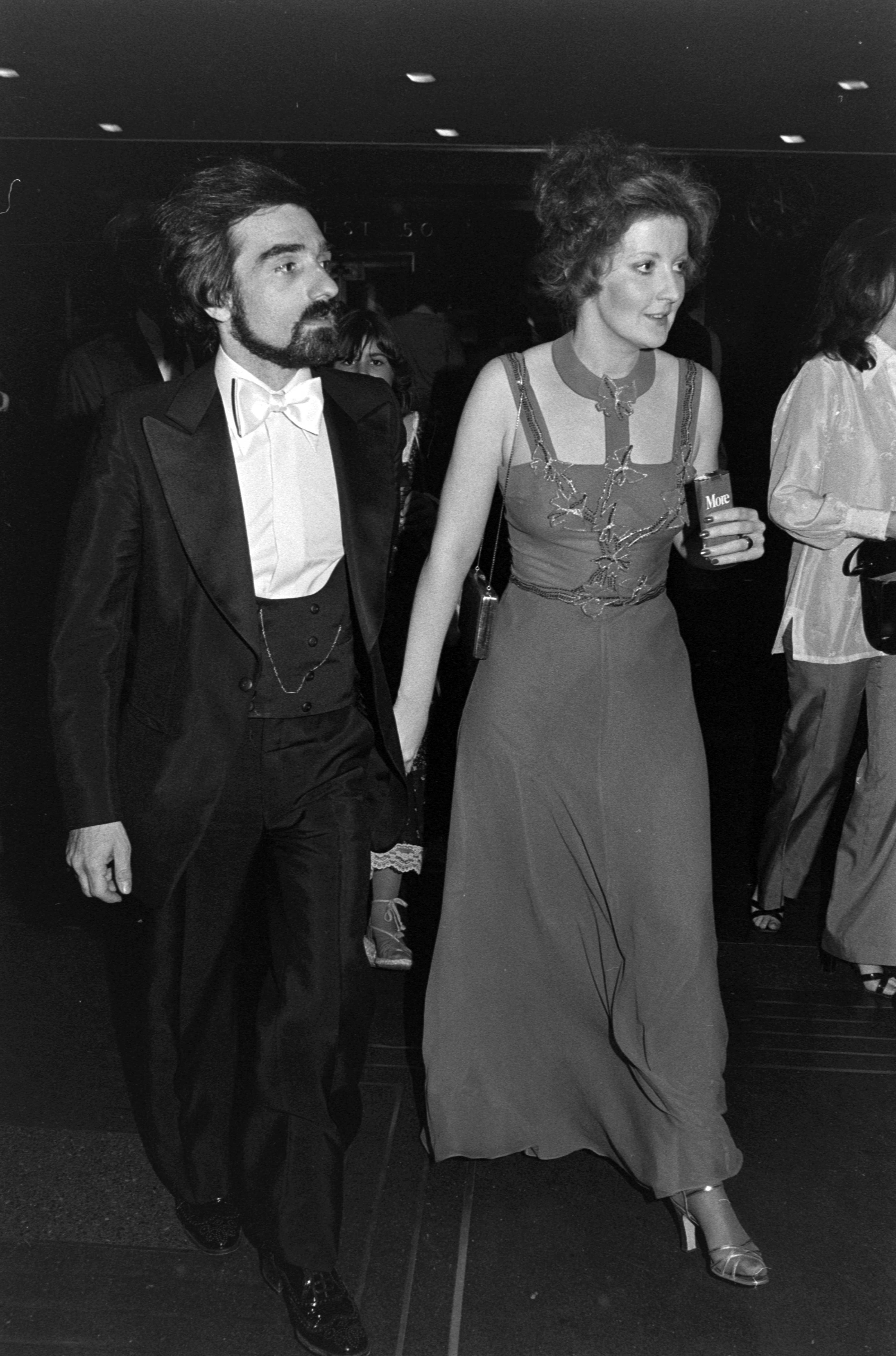 Martin Scorsese and Julia Cameron walking hand-in-hand, Scorsese in a classic tuxedo and Cameron in an elegant evening gown, at an event