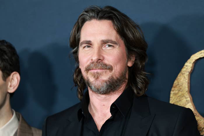 Christian Bale smiles while wearing a black suit at a formal event