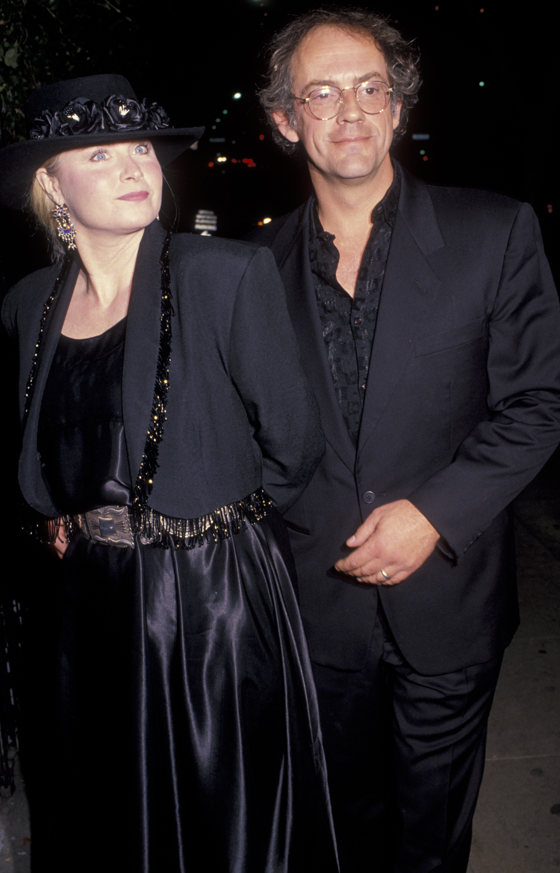 Mary Steenburgen in a wide-brimmed hat and satin outfit, and Christopher Lloyd in a suit, attend an event at night