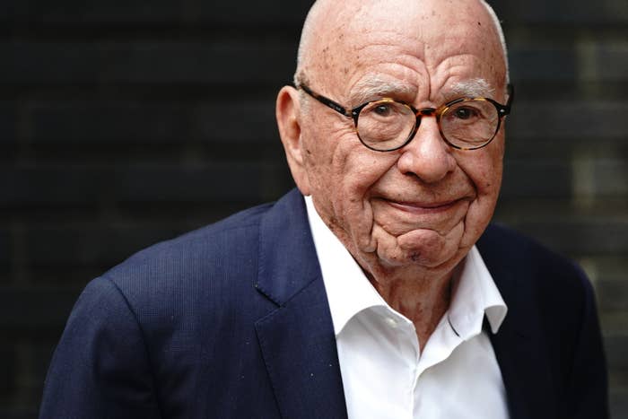 Rupert Murdoch wearing a white shirt and dark suit jacket, smiling slightly with a neutral background