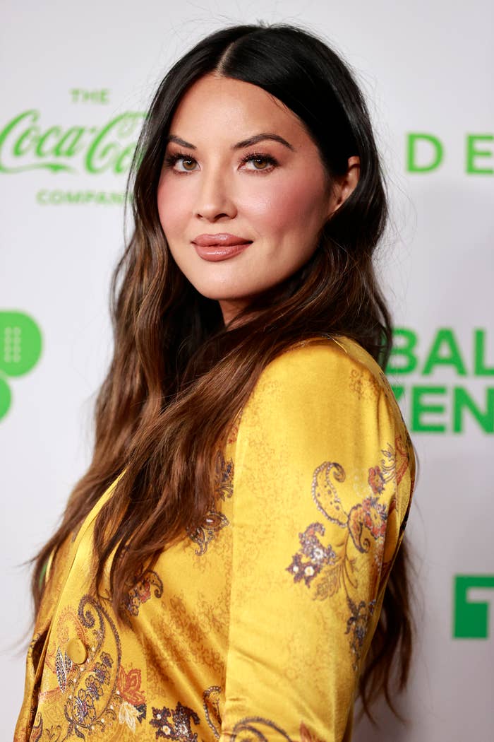 Olivia Munn poses on the red carpet in a patterned, golden jacket