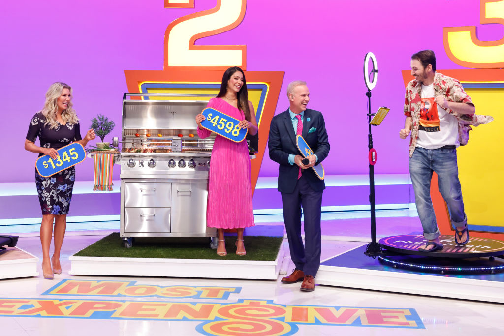 Contestants on The Price Is Right hold price tags and a BBQ grill. Drew Carey hosts, wearing a suit. A contestant jumps excitedly, wearing casual attire