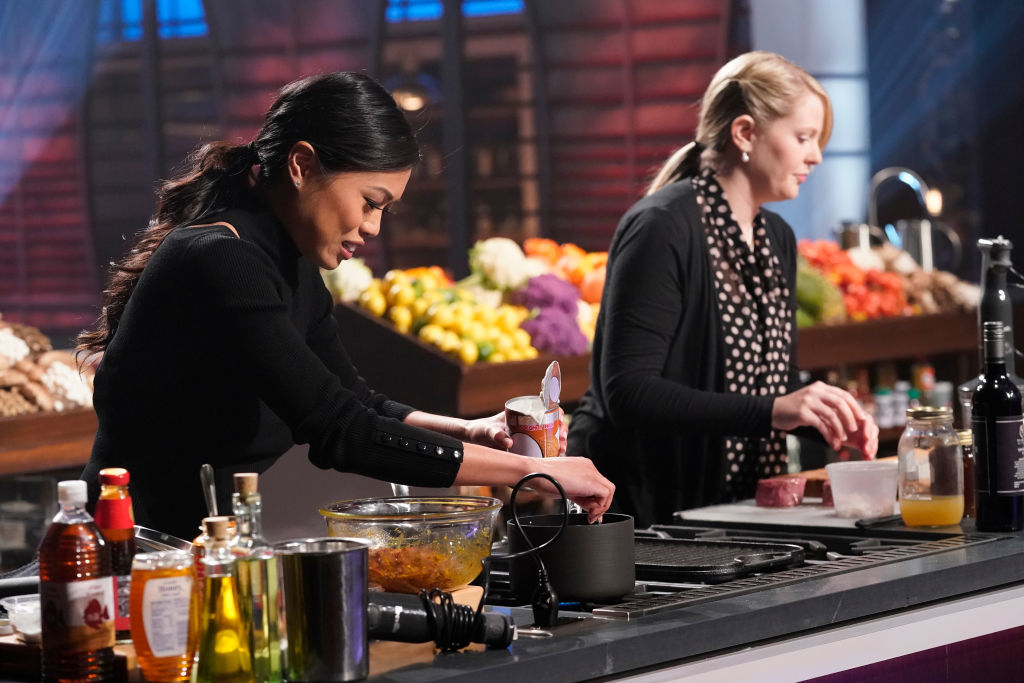 Two women cooking side by side at a professional kitchen station, focusing intently on their dishes