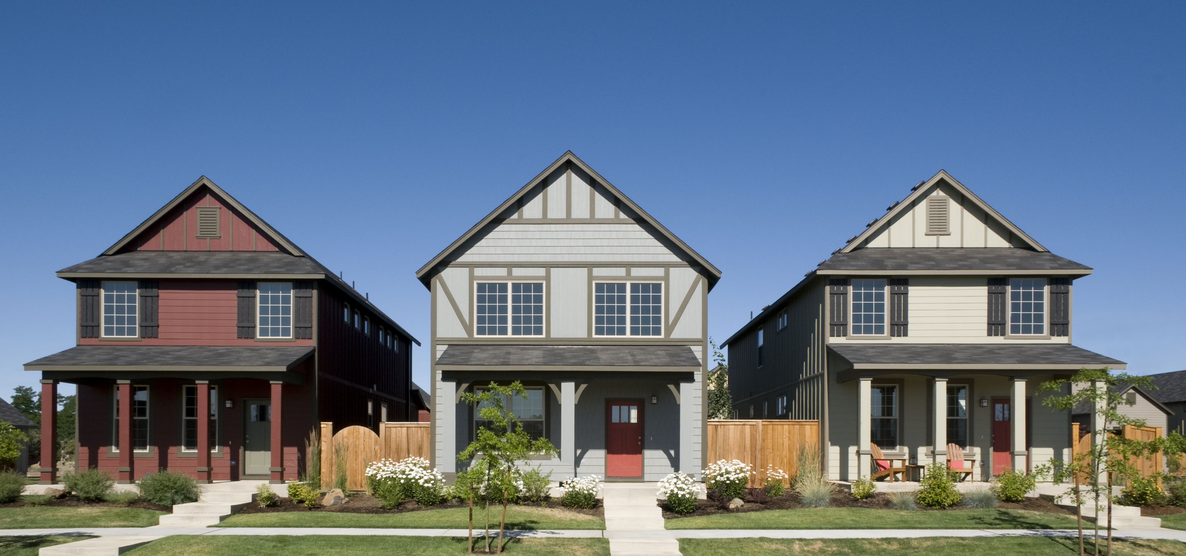 Three modern, two-story houses with front porches, each featuring a peaked roof and pathways leading to the entrances