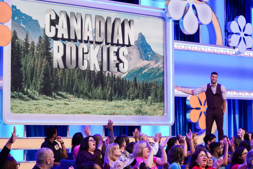 A game show set with a large screen showing the words &quot;Canadian Rockies&quot;. The host, John Michael Higgins, stands onstage with the audience cheering