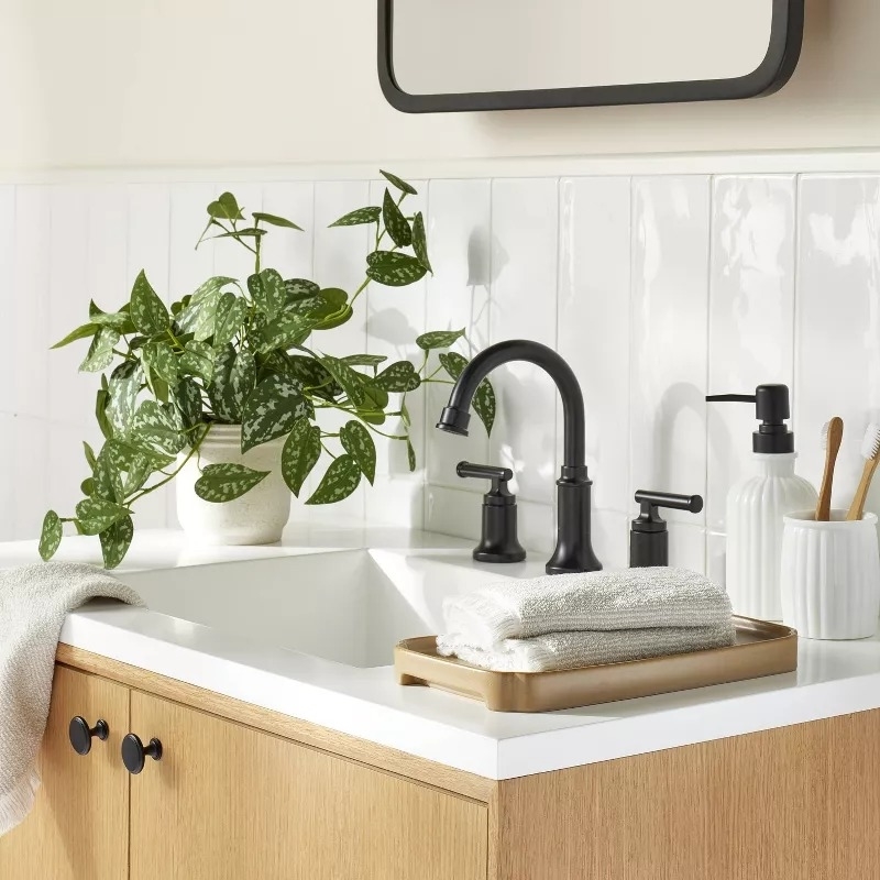 Stylish bathroom sink setup with black fixtures, a potted plant, and neatly folded towels on a tray, promoting home decor shopping