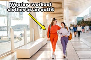 Two women walk and chat in a sunlit corridor, both dressed in vibrant workout clothes. An arrow points to them with the text "Wearing workout clothes as an outfit."