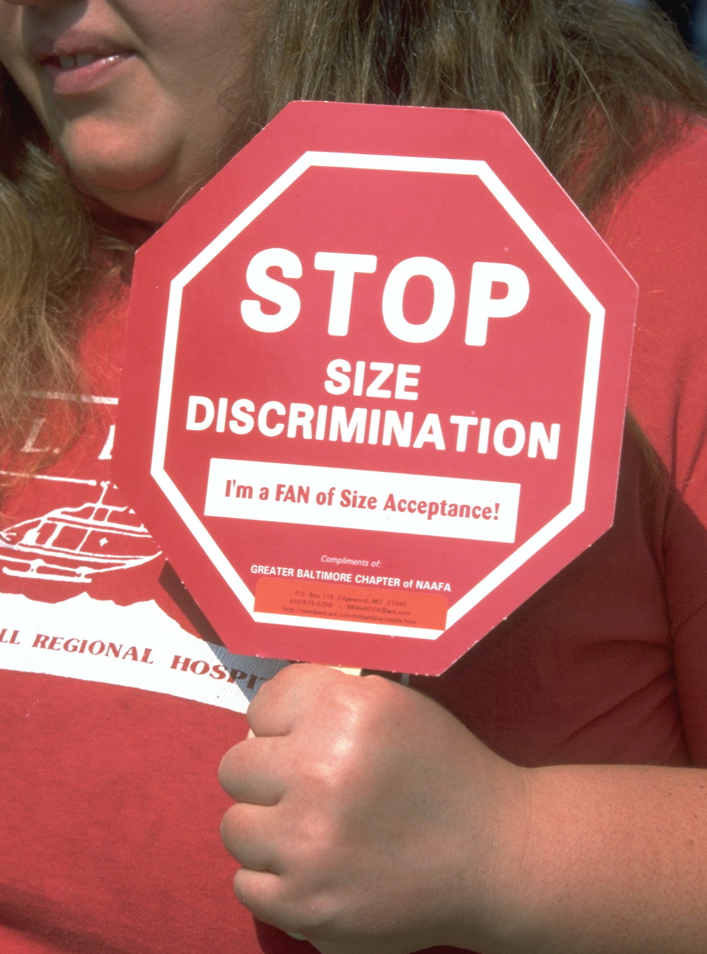 A person holds a sign that reads, "STOP SIZE DISCRIMINATION. I'm a FAN of Size Acceptance!"