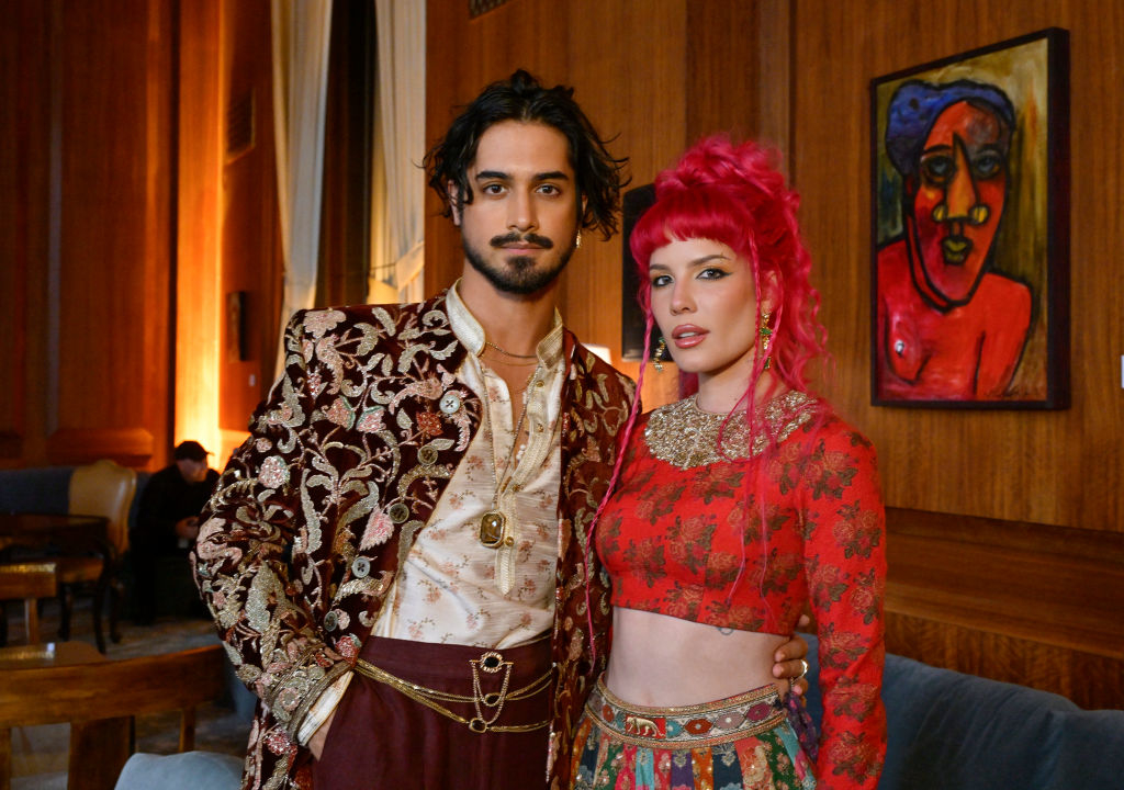 Avan Jogia and Halsey pose together; Avan wears an ornate jacket with intricate patterns, while Halsey rocks vibrant hair and a detailed two-piece outfit