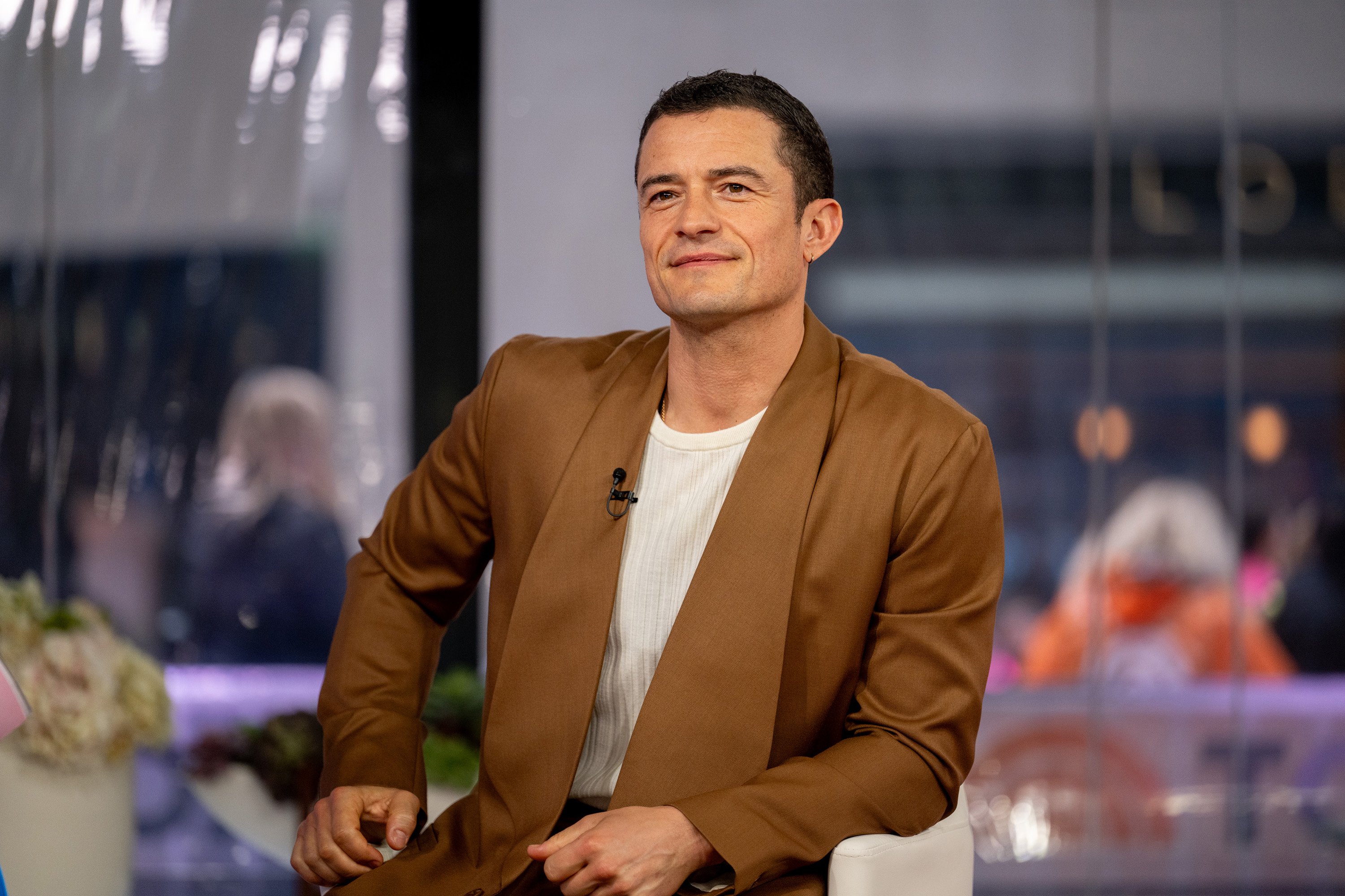 Orlando Bloom wearing a brown jacket over a white shirt, sitting for an interview