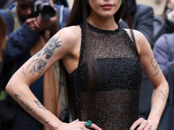 Halsey poses confidently in a sleeveless mesh dress with intricate tattooed arms on display, surrounded by photographers
