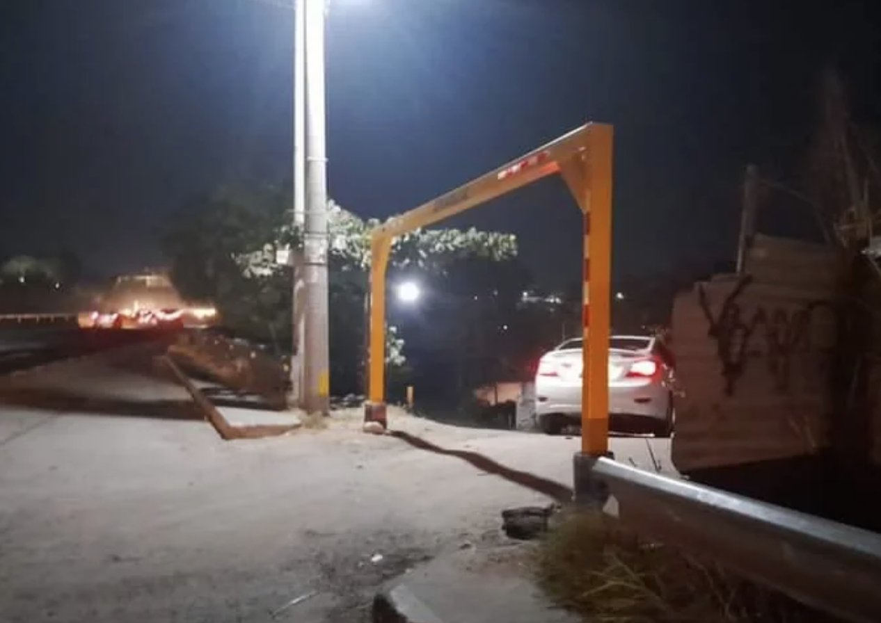 Car narrowly avoids hitting a horizontally installed elevated barrier pole blocking part of a road at night
