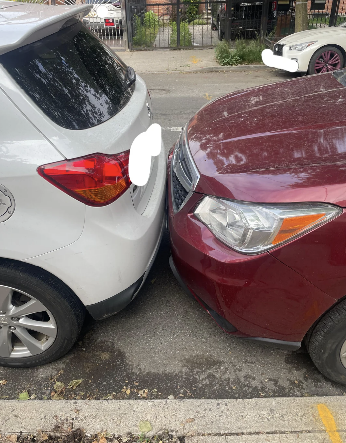 Two cars parked closely, bumper to bumper on a street. The front of a maroon car touches the back of a white car