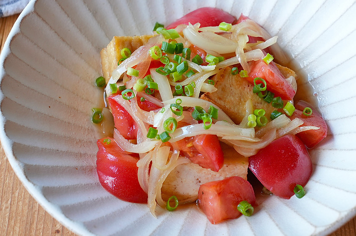 白い皿に盛られたトマトと玉ねぎを使った料理。細かく刻んだネギが上に散らされている。