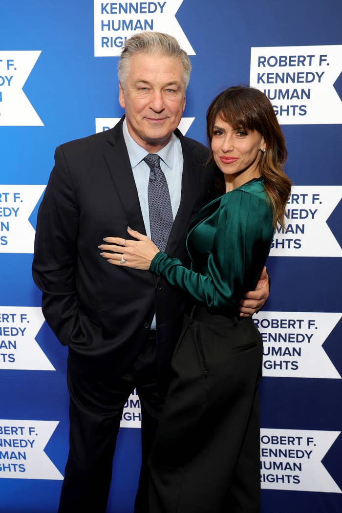 Alec Baldwin in a suit and Hilaria Baldwin in a long-sleeve satin dress at the Robert F. Kennedy Human Rights event, posing in front of a step-and-repeat backdrop