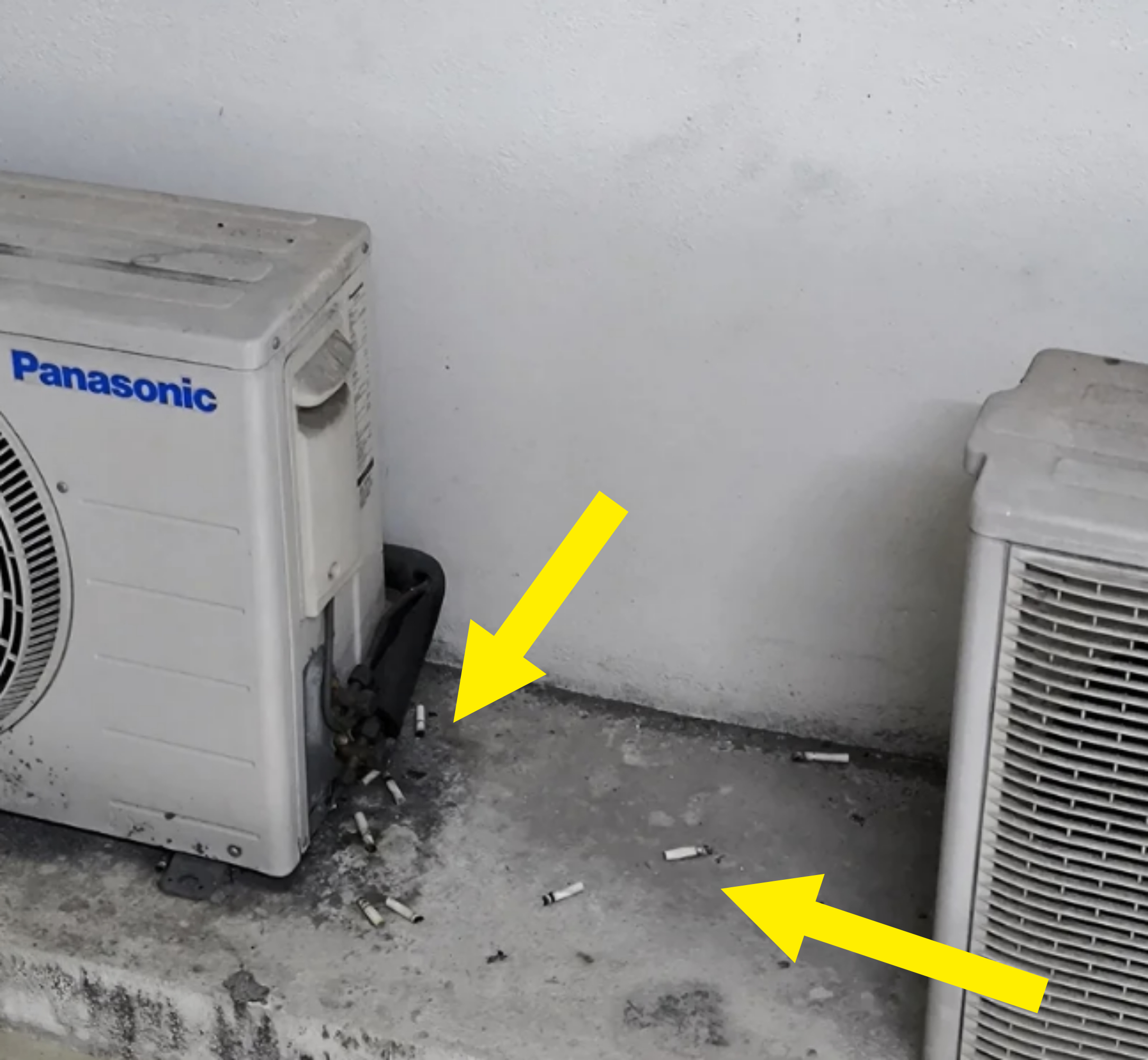 Two Panasonic outdoor air conditioning units on a concrete surface, surrounded by scattered cigarette butts